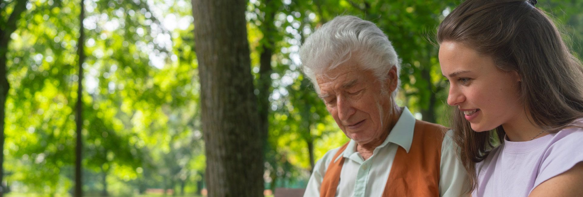An older man talking with an younger woman on a park bench