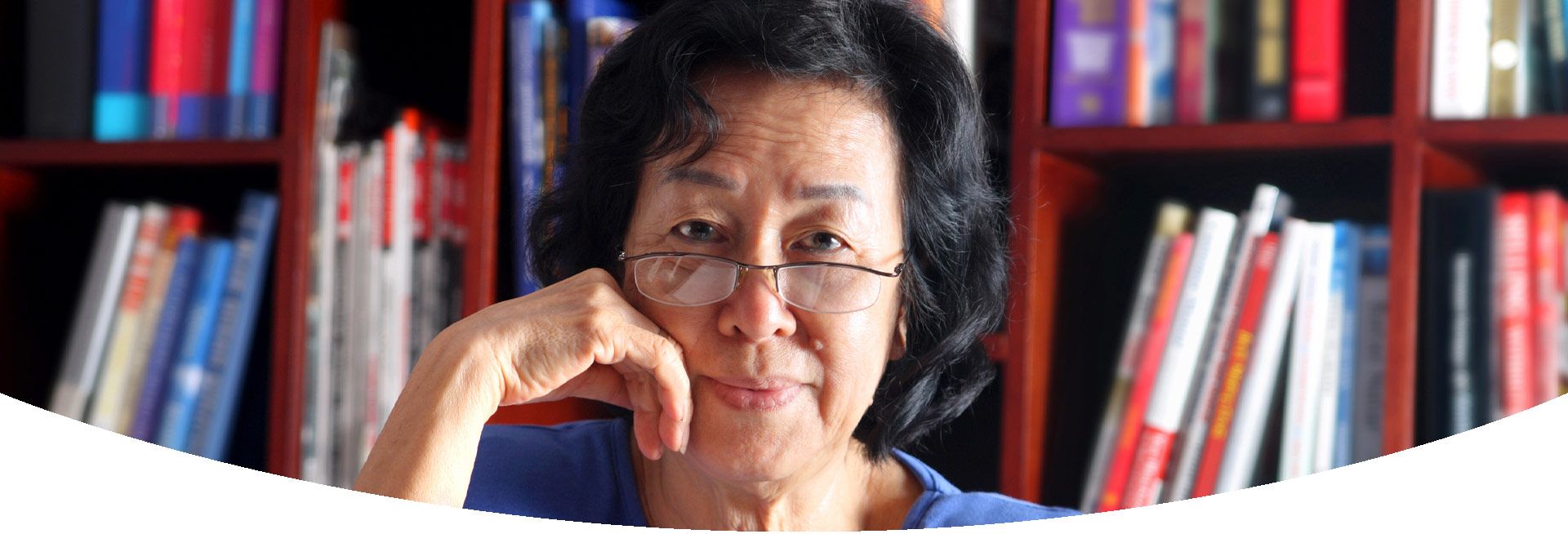 Older Asian woman posing in front of a bookcase full of books