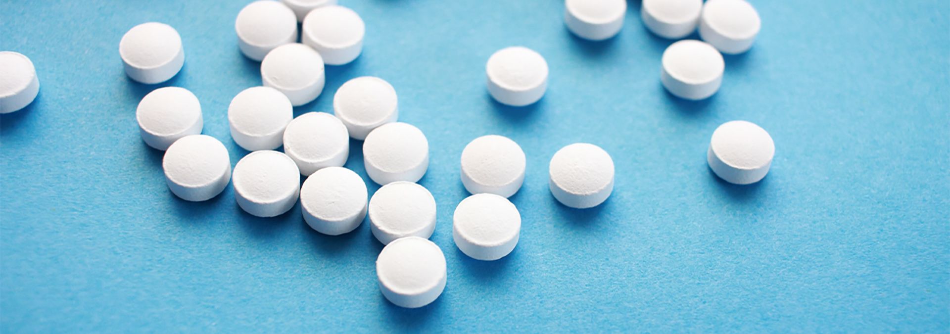 Close up photo of several white circular pills on a soft blue surface