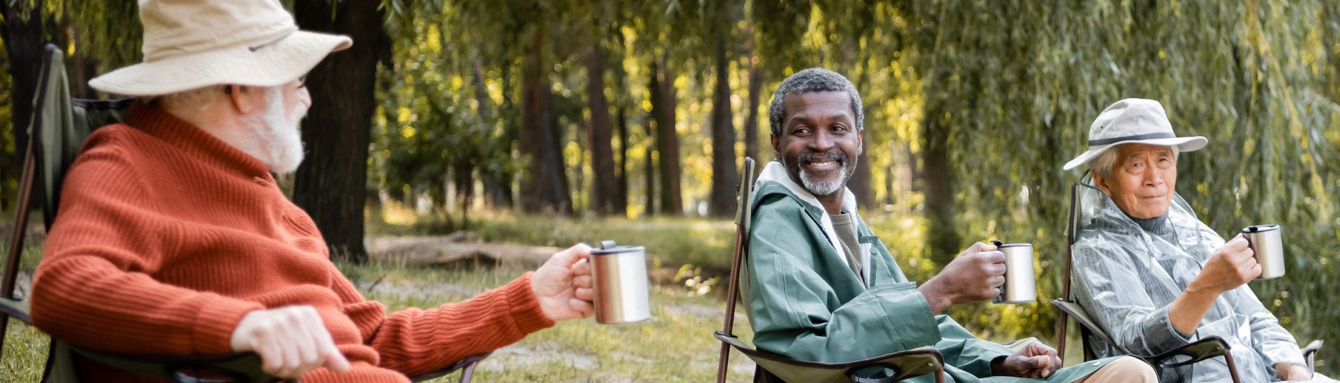 Group of elderly men friends outside at a lake sitting down drinking coffee